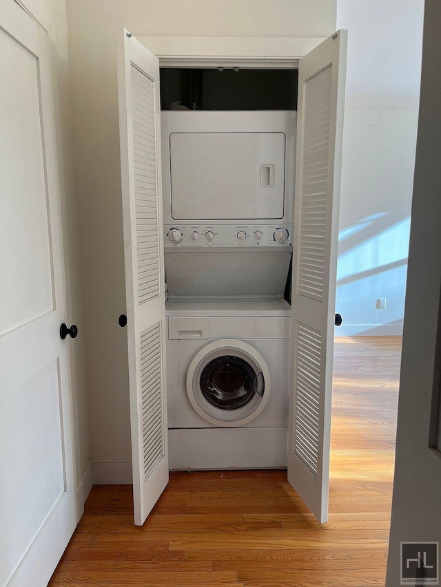 laundry area with stacked washer and dryer, wood finished floors, and laundry area