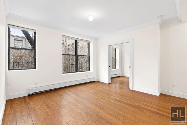 empty room with baseboard heating, plenty of natural light, crown molding, and light wood-type flooring