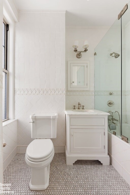 full bathroom featuring tile walls, shower / bath combination with glass door, tile patterned flooring, vanity, and toilet