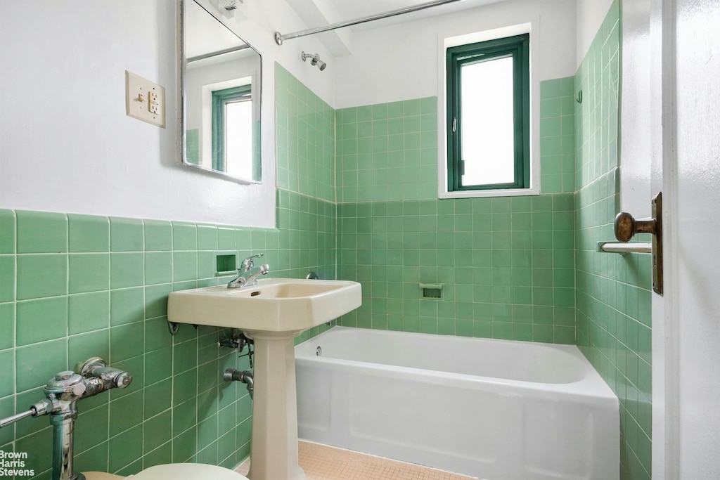 bathroom featuring toilet, washtub / shower combination, tile walls, and wainscoting