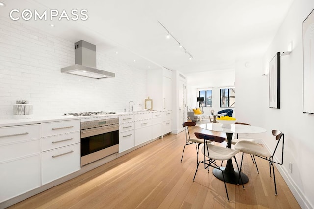 kitchen with wall chimney exhaust hood, white cabinetry, white gas cooktop, oven, and light hardwood / wood-style floors