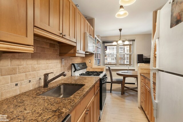 kitchen with decorative light fixtures, tasteful backsplash, sink, dark stone countertops, and white appliances