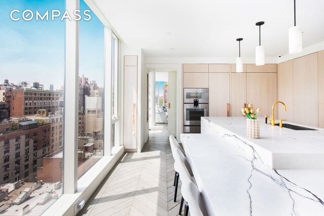 kitchen with modern cabinets, light stone counters, hanging light fixtures, stainless steel double oven, and a sink