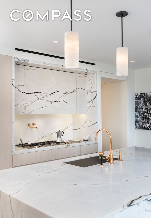 kitchen featuring backsplash, a sink, gas stovetop, and decorative light fixtures