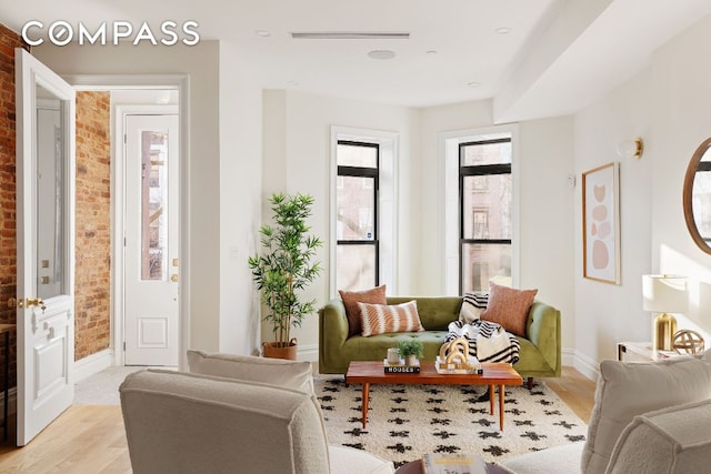 living room featuring brick wall, light wood-style flooring, and baseboards