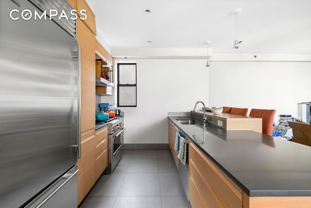 kitchen with a peninsula, premium appliances, dark countertops, and a sink