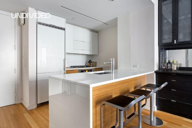 kitchen featuring a breakfast bar, sink, built in refrigerator, light wood-type flooring, and kitchen peninsula