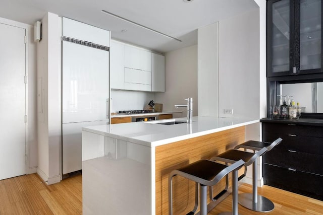 kitchen with sink, a kitchen breakfast bar, built in refrigerator, kitchen peninsula, and light wood-type flooring