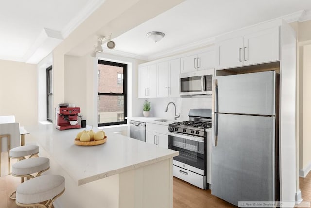 kitchen with sink, a breakfast bar, appliances with stainless steel finishes, white cabinetry, and ornamental molding