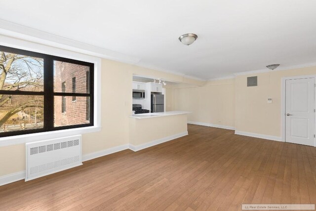 unfurnished living room with radiator, wood-type flooring, and plenty of natural light