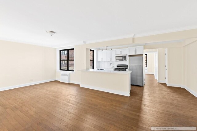 kitchen with dark wood-type flooring, white cabinetry, radiator heating unit, stainless steel appliances, and kitchen peninsula