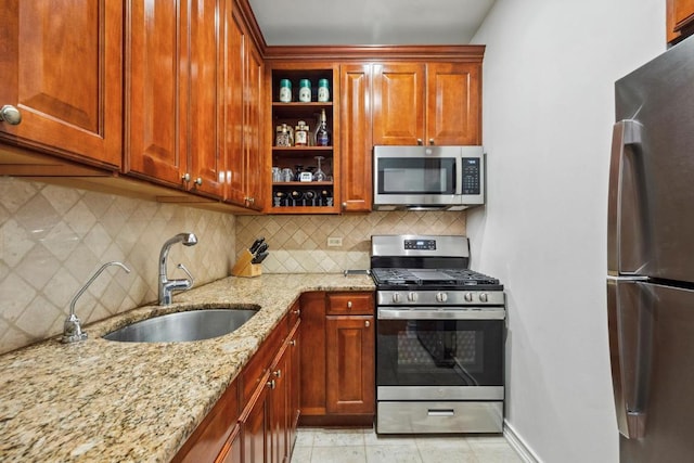 kitchen with appliances with stainless steel finishes, sink, light stone counters, and decorative backsplash