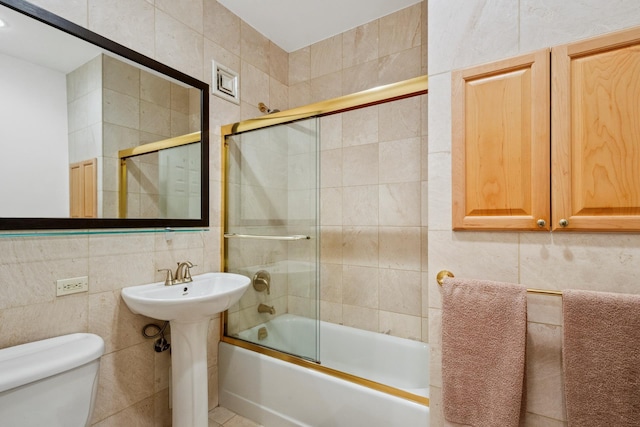 full bathroom featuring tile walls, toilet, shower / bath combination with glass door, and a sink