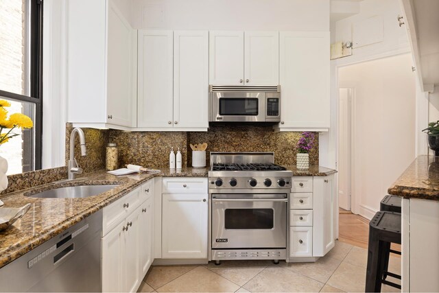 kitchen with white cabinetry, stainless steel appliances, sink, and dark stone counters