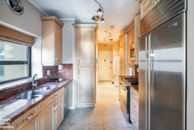 kitchen featuring light tile patterned floors, stainless steel appliances, a sink, backsplash, and dark stone counters