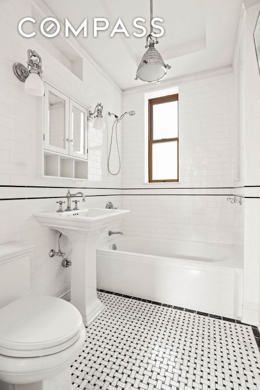 bathroom with tile walls, tiled shower / bath combo, a tray ceiling, and toilet