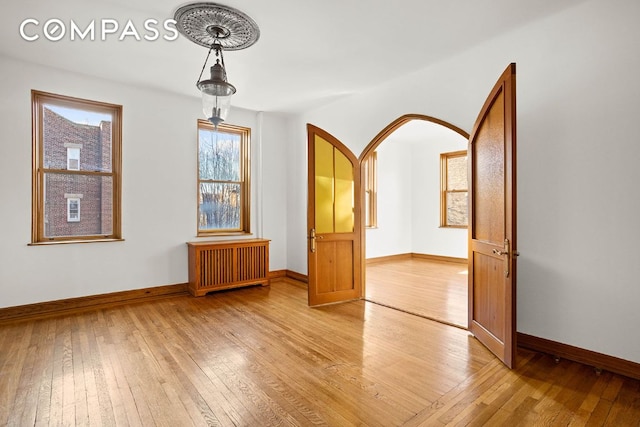 empty room with baseboards, light wood-style floors, arched walkways, and radiator