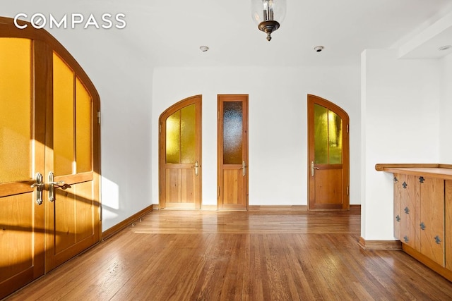 empty room featuring arched walkways, wood finished floors, and baseboards