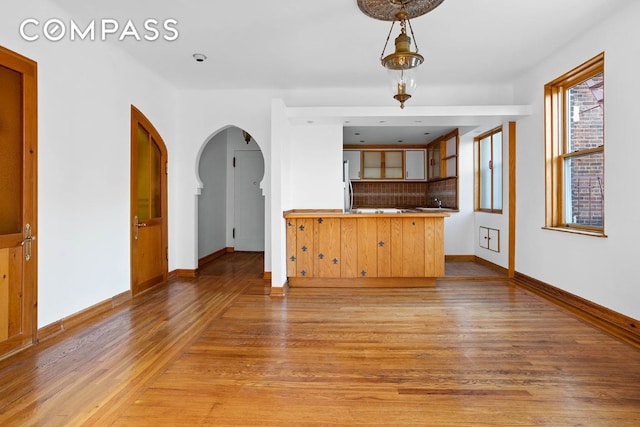 interior space featuring backsplash, fridge, decorative light fixtures, kitchen peninsula, and light wood-type flooring