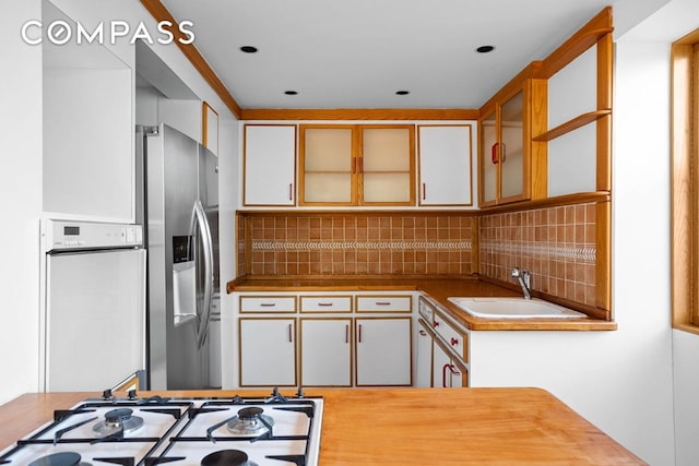 kitchen with white cabinetry, sink, stainless steel fridge, decorative backsplash, and gas stovetop