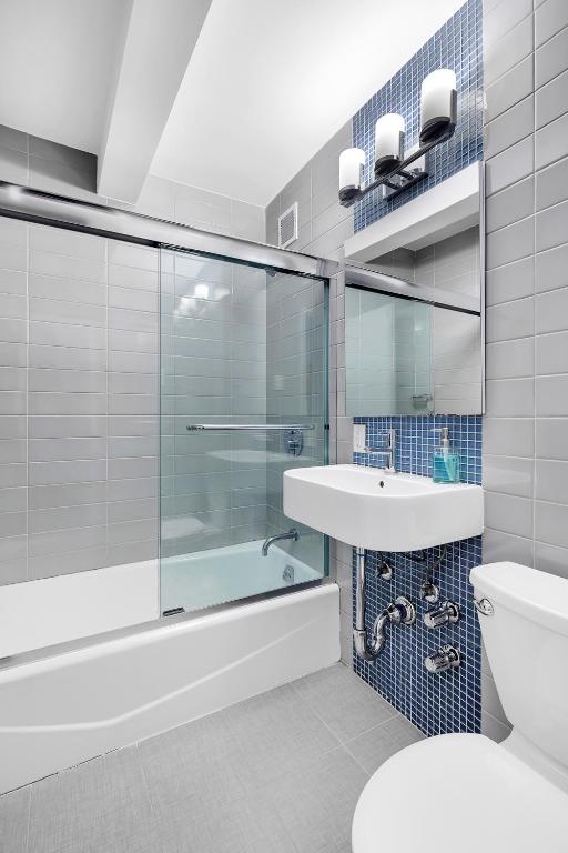 full bathroom featuring tile patterned flooring, tile walls, shower / bath combination with glass door, and toilet