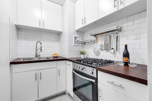 kitchen featuring stainless steel gas range, a sink, butcher block counters, backsplash, and white cabinets