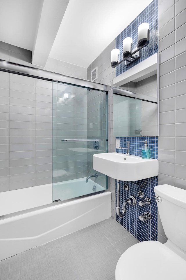 bathroom featuring tile walls, toilet, combined bath / shower with glass door, tile patterned flooring, and backsplash