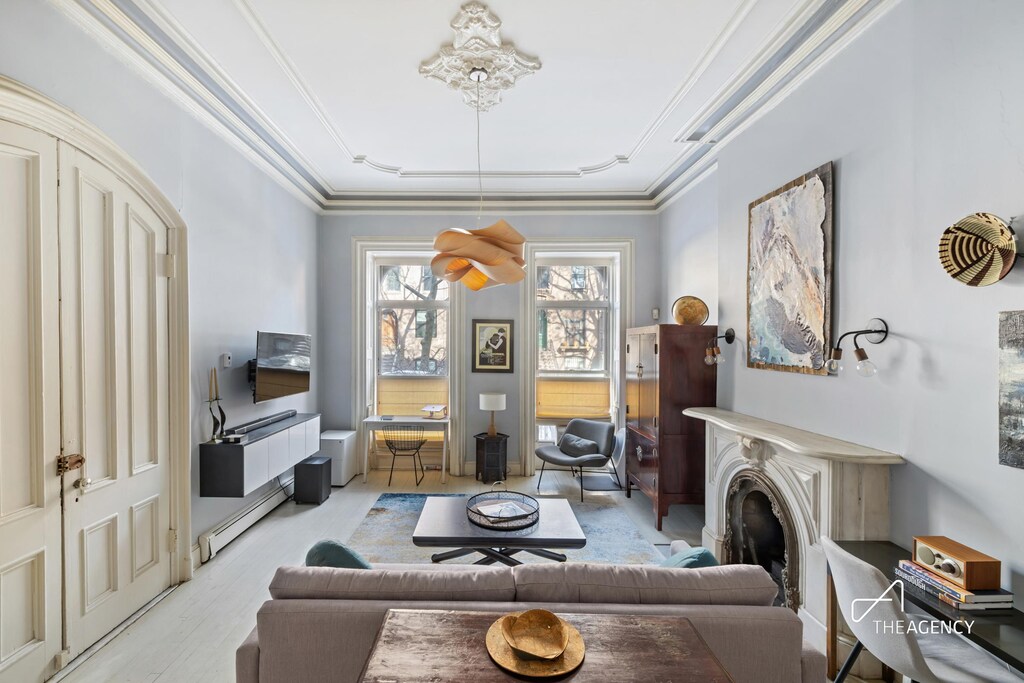 living area featuring a baseboard heating unit, a fireplace, light wood finished floors, and ornamental molding