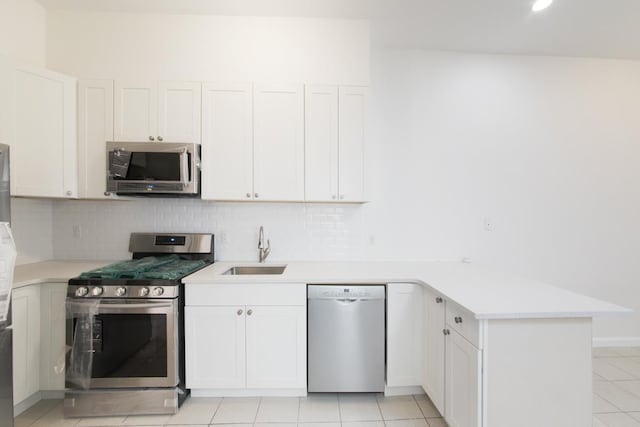 kitchen featuring a sink, backsplash, appliances with stainless steel finishes, a peninsula, and light countertops