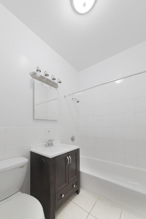 full bathroom with tile walls, tiled shower / bath combo, vanity, toilet, and tile patterned floors