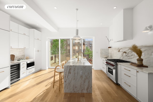 kitchen with hanging light fixtures, stainless steel stove, beverage cooler, and white cabinets