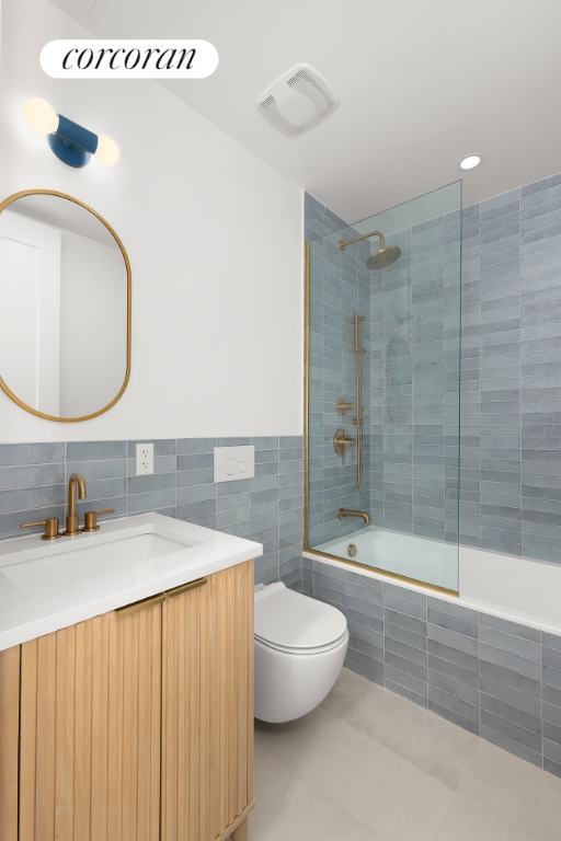 full bathroom featuring tile patterned floors, toilet, tiled shower / bath, tile walls, and vanity