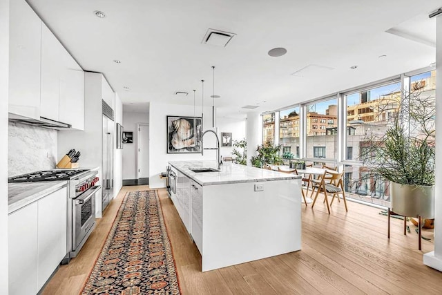 kitchen with pendant lighting, sink, white cabinetry, stainless steel range, and an island with sink