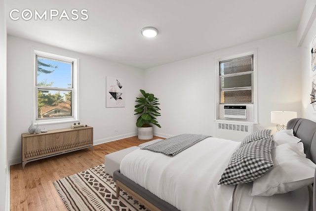 bedroom with baseboards, light wood-style flooring, radiator heating unit, and cooling unit