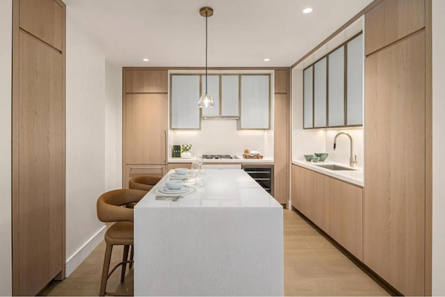 kitchen with sink, hanging light fixtures, a kitchen breakfast bar, a center island, and light hardwood / wood-style floors