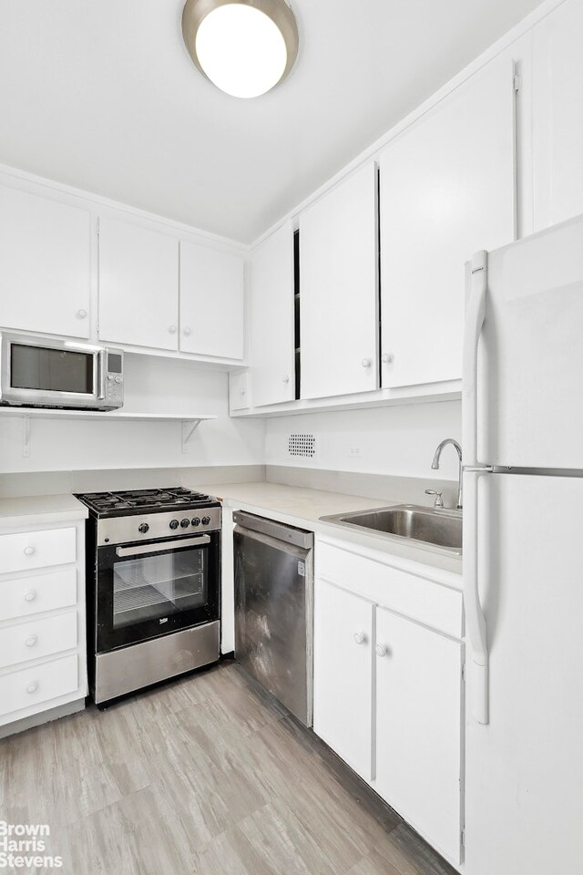 kitchen featuring appliances with stainless steel finishes, light countertops, a sink, and white cabinetry