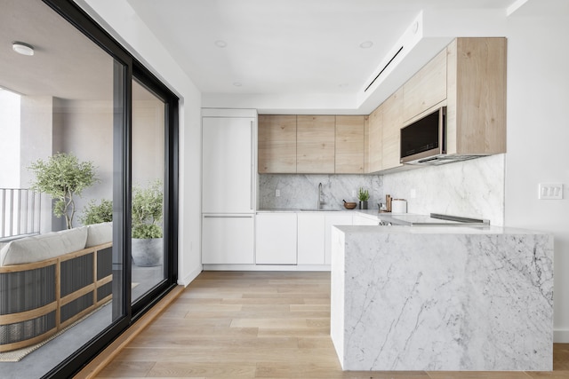 kitchen featuring a sink, light countertops, light wood-type flooring, stainless steel microwave, and modern cabinets