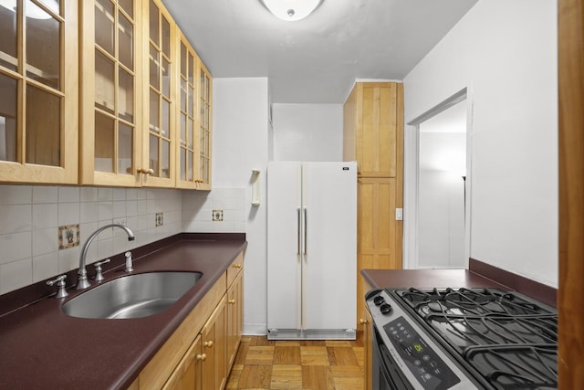 kitchen with dark countertops, decorative backsplash, freestanding refrigerator, stainless steel gas range, and a sink