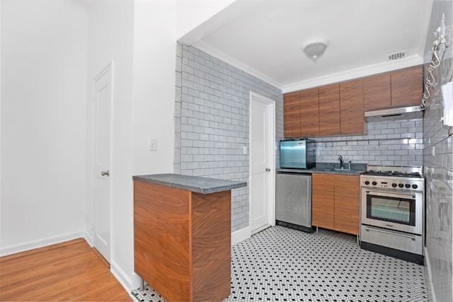 kitchen featuring dark countertops, appliances with stainless steel finishes, brown cabinetry, ornamental molding, and a sink