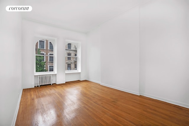 unfurnished room with radiator, wood-type flooring, visible vents, and baseboards