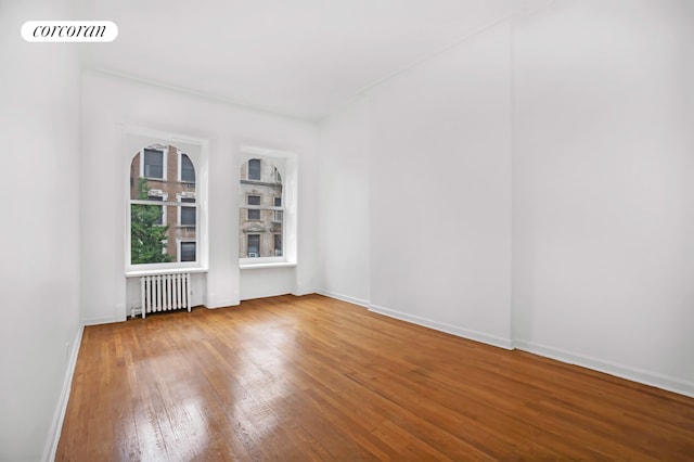 empty room featuring baseboards, visible vents, radiator heating unit, and wood finished floors
