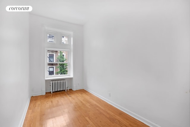 empty room featuring light wood-style floors, baseboards, radiator heating unit, and visible vents