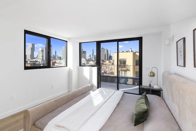 bedroom with a city view, wood finished floors, baseboards, and access to outside