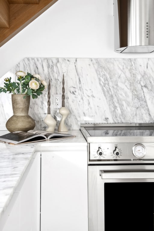 room details with stove, backsplash, white cabinetry, and wall chimney exhaust hood