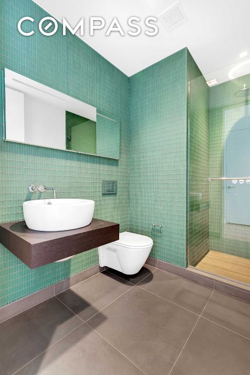 bathroom with tile walls, a shower with door, tile patterned floors, and toilet