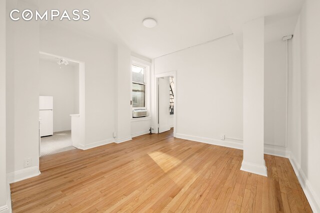 spare room featuring cooling unit, light wood-style flooring, and baseboards