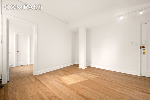 empty room featuring track lighting, baseboards, and light wood finished floors