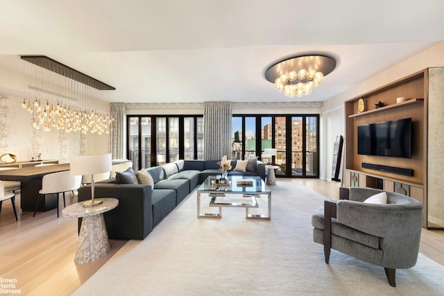 living room with a notable chandelier, french doors, and light wood-type flooring