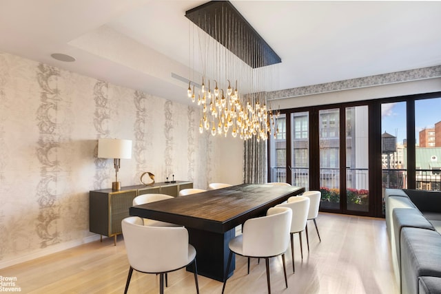 dining area with wallpapered walls, light wood finished floors, baseboards, a city view, and a notable chandelier