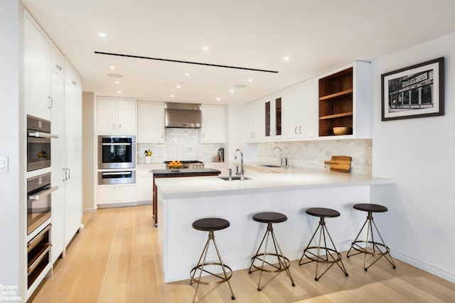 kitchen featuring white cabinets, sink, kitchen peninsula, and wall chimney range hood